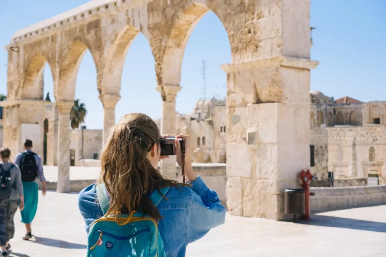 Traveler photographing ancient stone archway and historical destination.