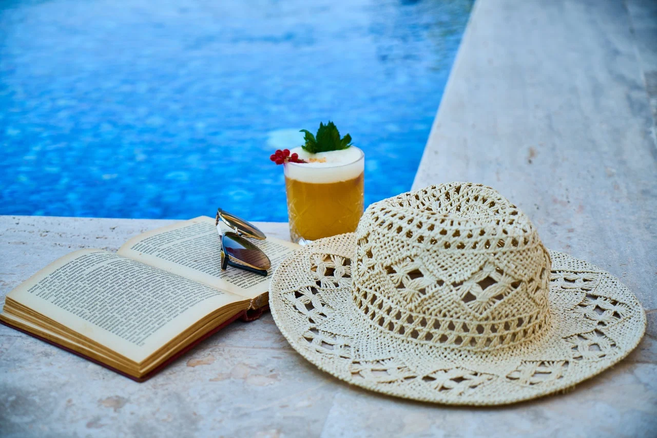 a pair of glasses with a drink and a straw on a towel by a pool