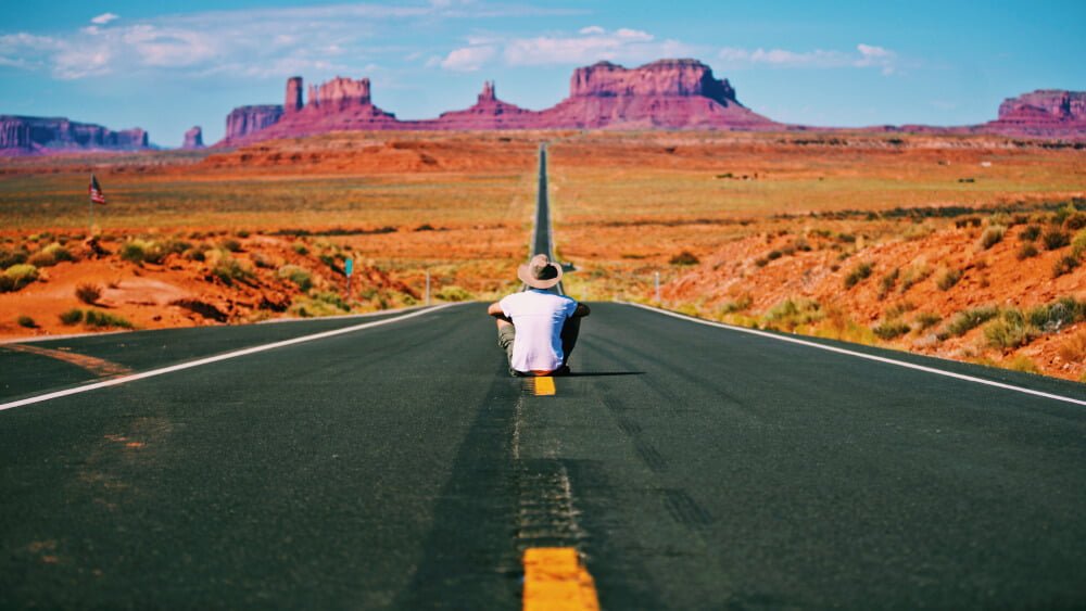 a person sitting on a road with a tall tower in the background