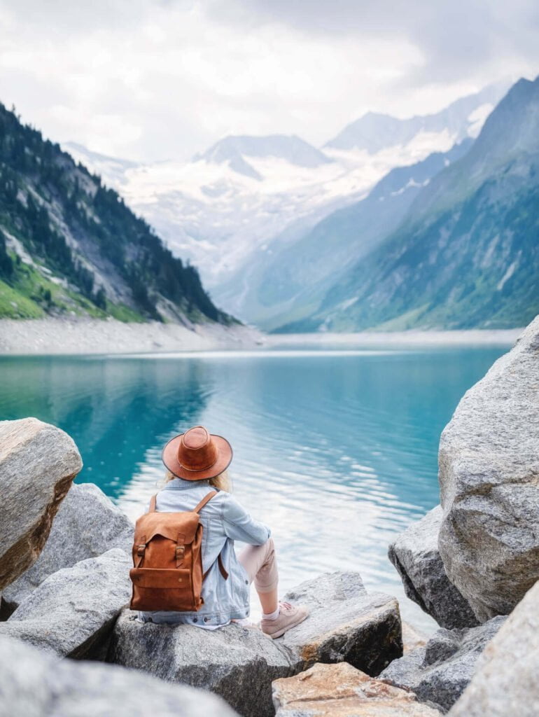 a person sitting on a rock by a lake with mountains in the background