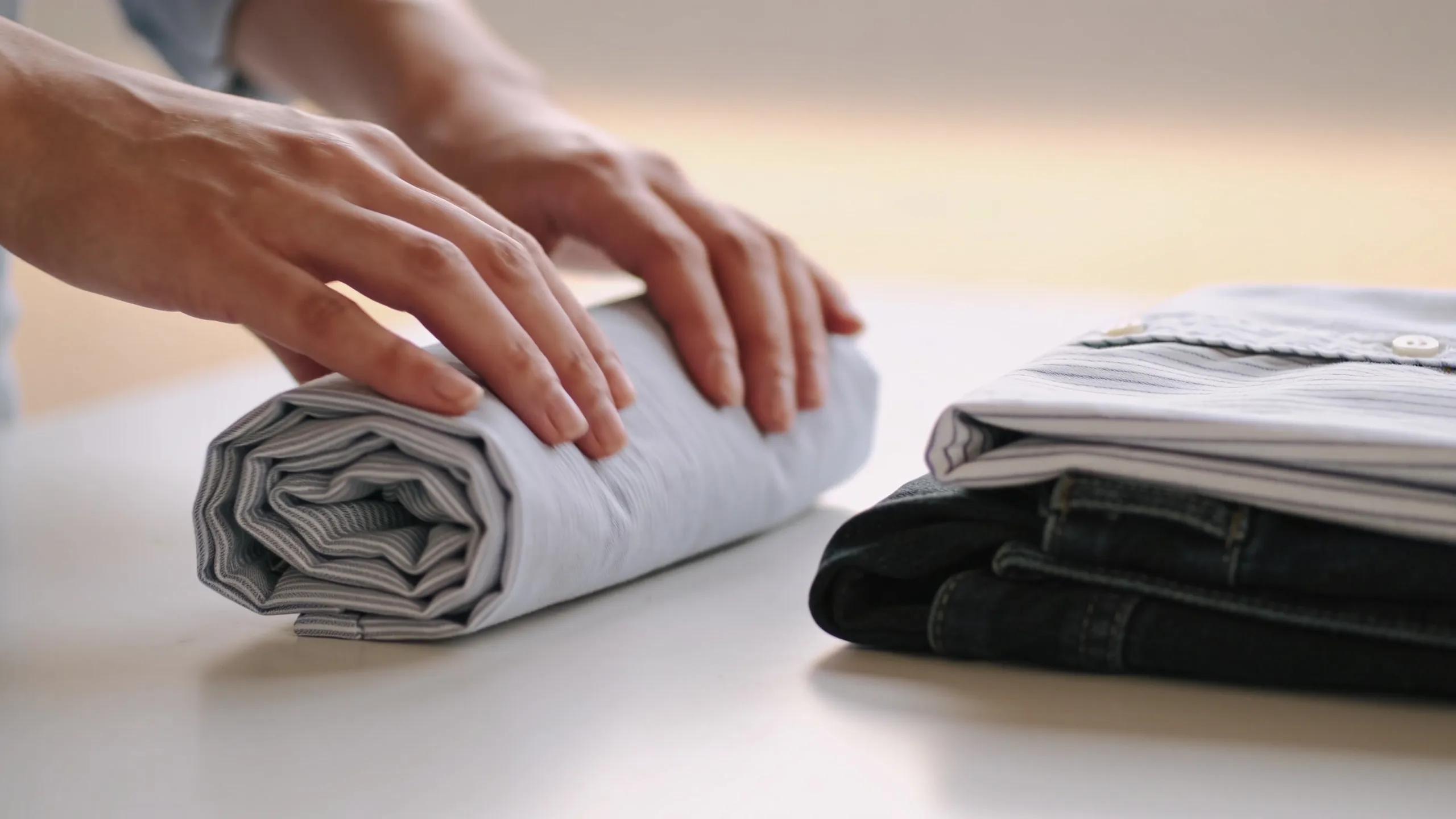 Person demonstrating rolling technique for packing clothes to save space and minimize wrinkles